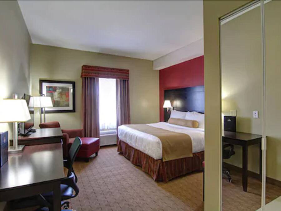 A hotel room with a bed, desk, chair, and a window with curtains.