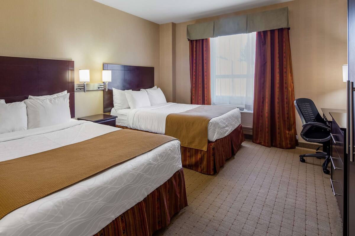 A hotel room with two beds, a desk, a chair, and a window with curtains.