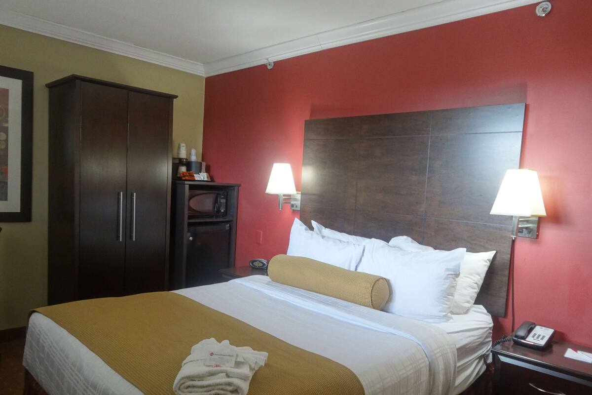 A hotel room with a bed, two bedside lamps, a nightstand, a telephone, a microwave, and a cabinet.