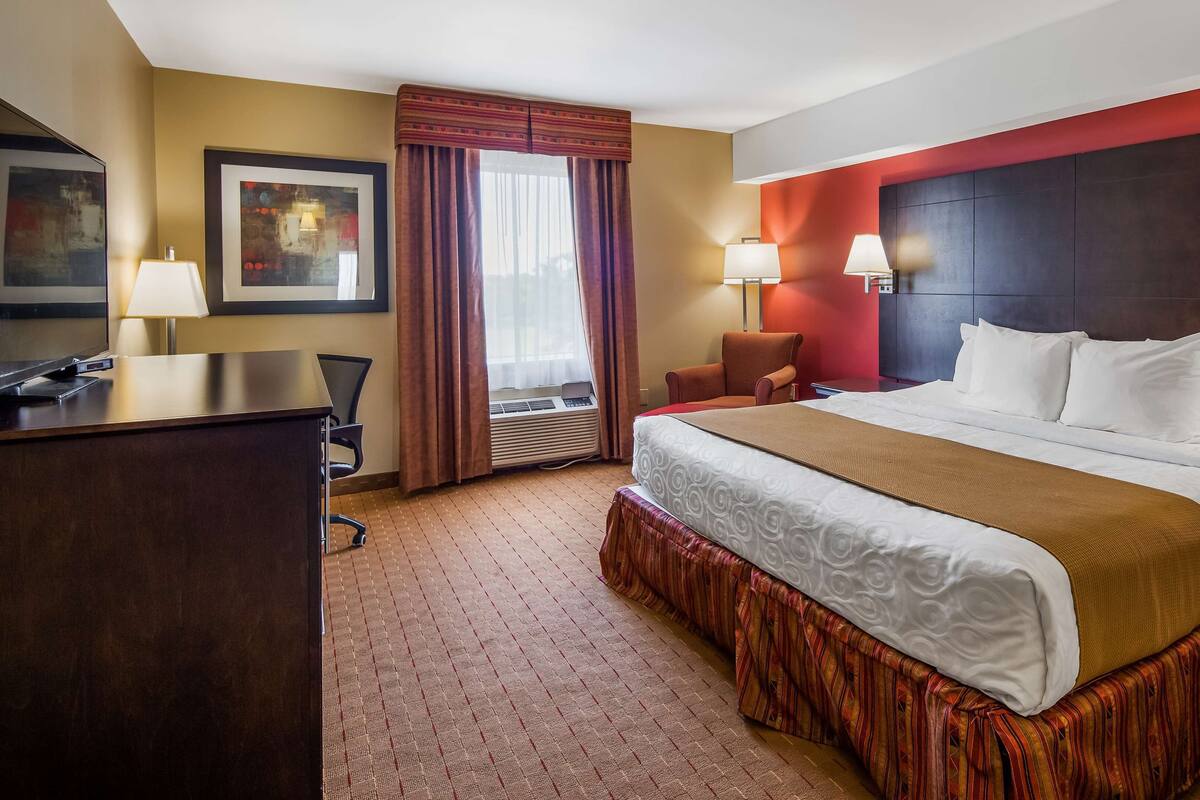 A hotel room with a large bed, a desk, a chair, and a TV.