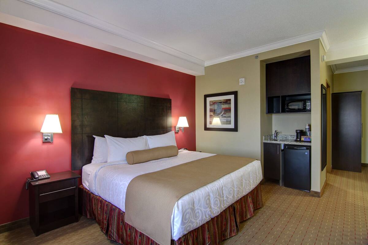 A hotel room with a bed, bedside lamps, a small desk with a phone, a microwave, and a refrigerator.