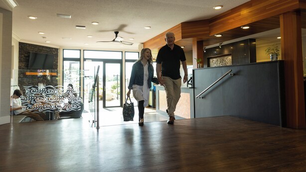 A modern lobby with a wooden floor, a reception desk, and a seating area with a decorative wall.