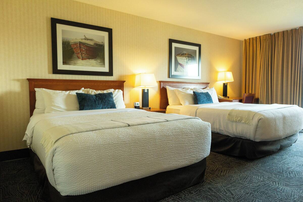 A hotel room with two beds, each with a headboard, bedside lamps, and framed artwork on the wall.