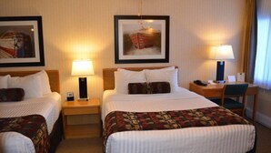 A hotel room with two beds, a desk, and a chair. There are two lamps on the nightstands.