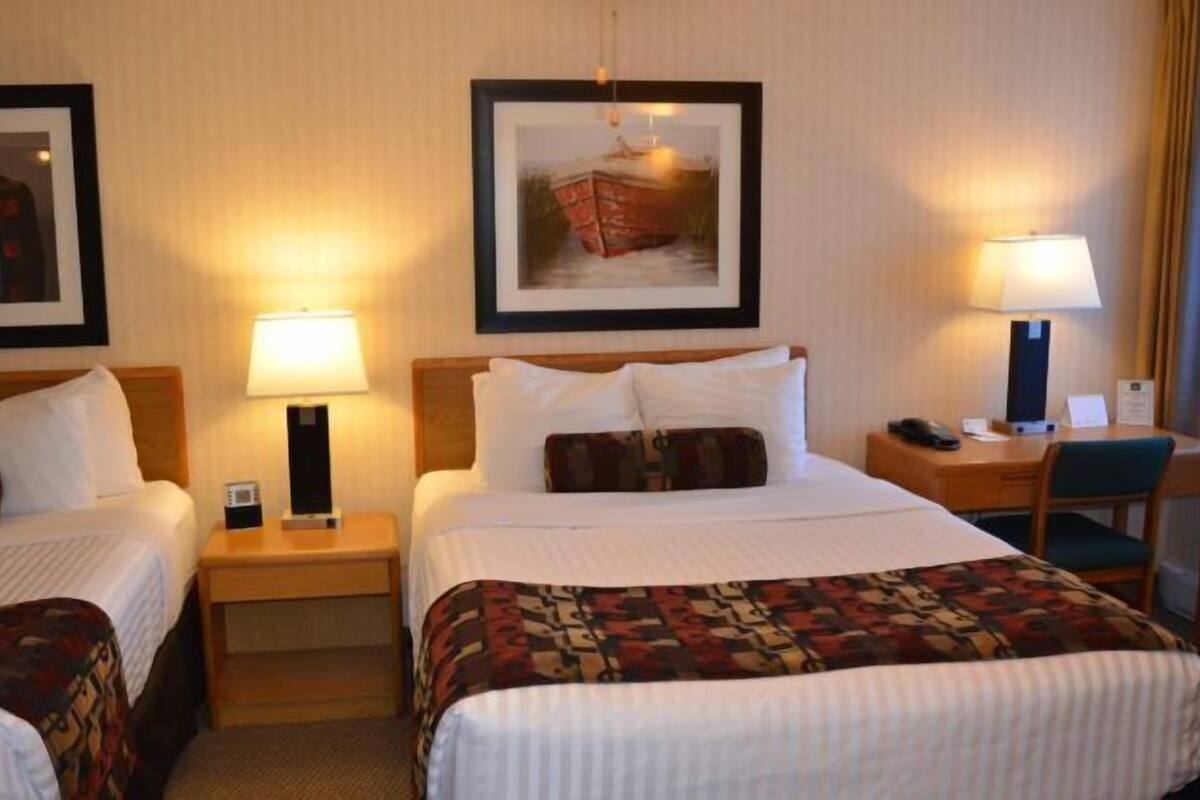 A hotel room with two beds, a desk, and a chair. There are two lamps on the nightstands.