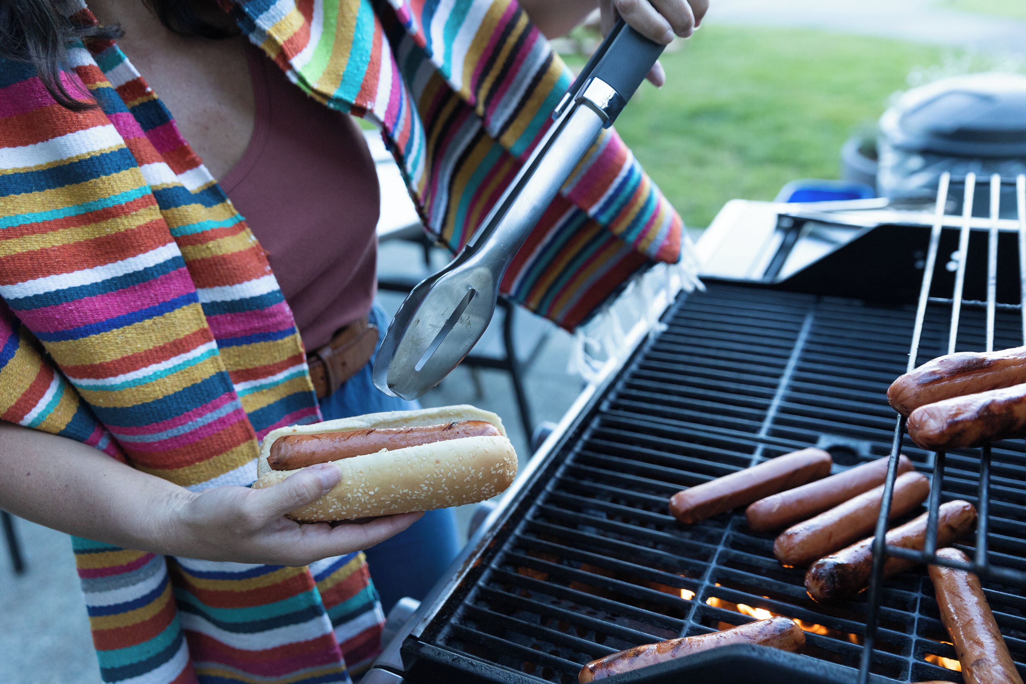 A person grilling hot dogs on an outdoor grill.