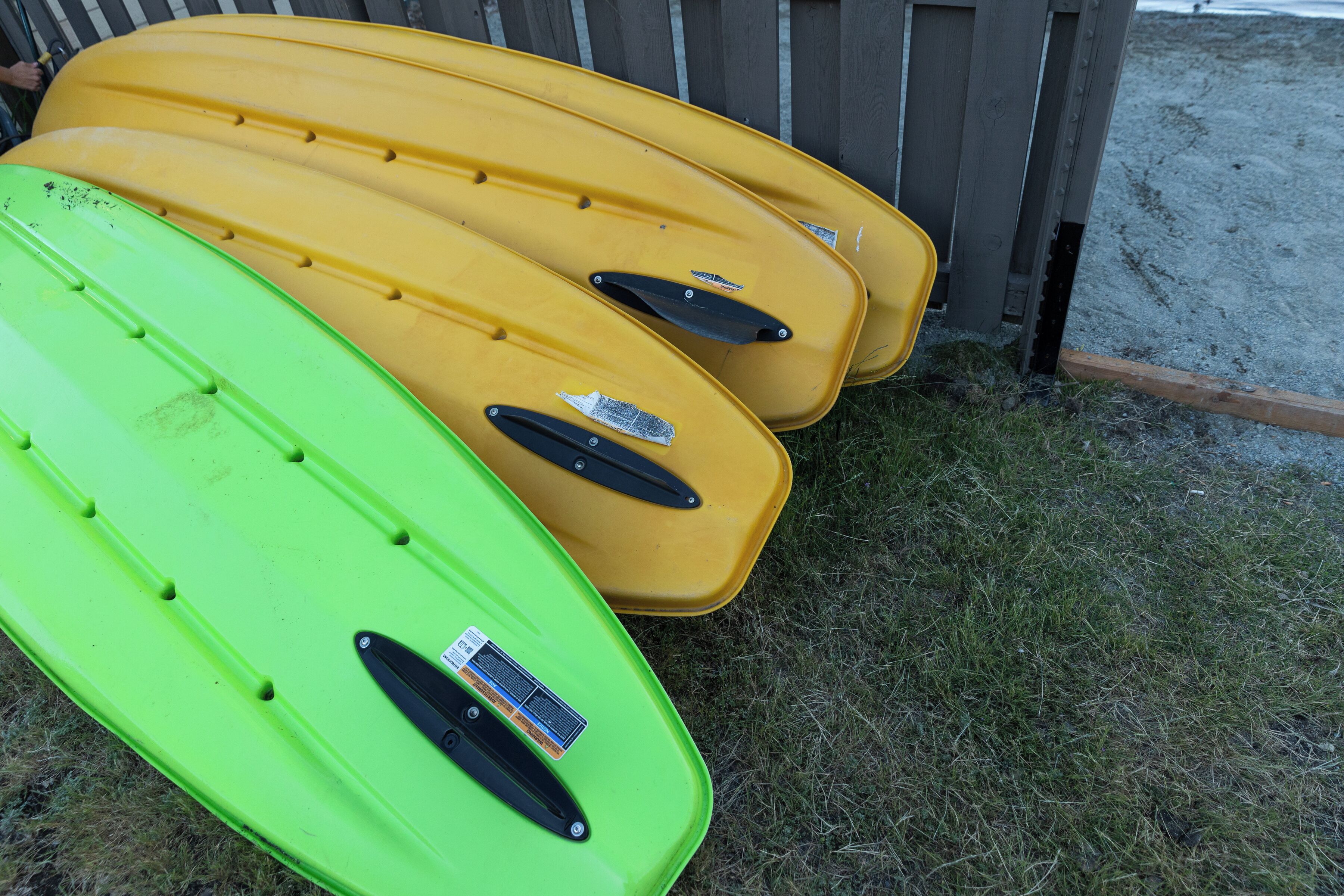 Tres kayaks alineados junto a una valla de madera.