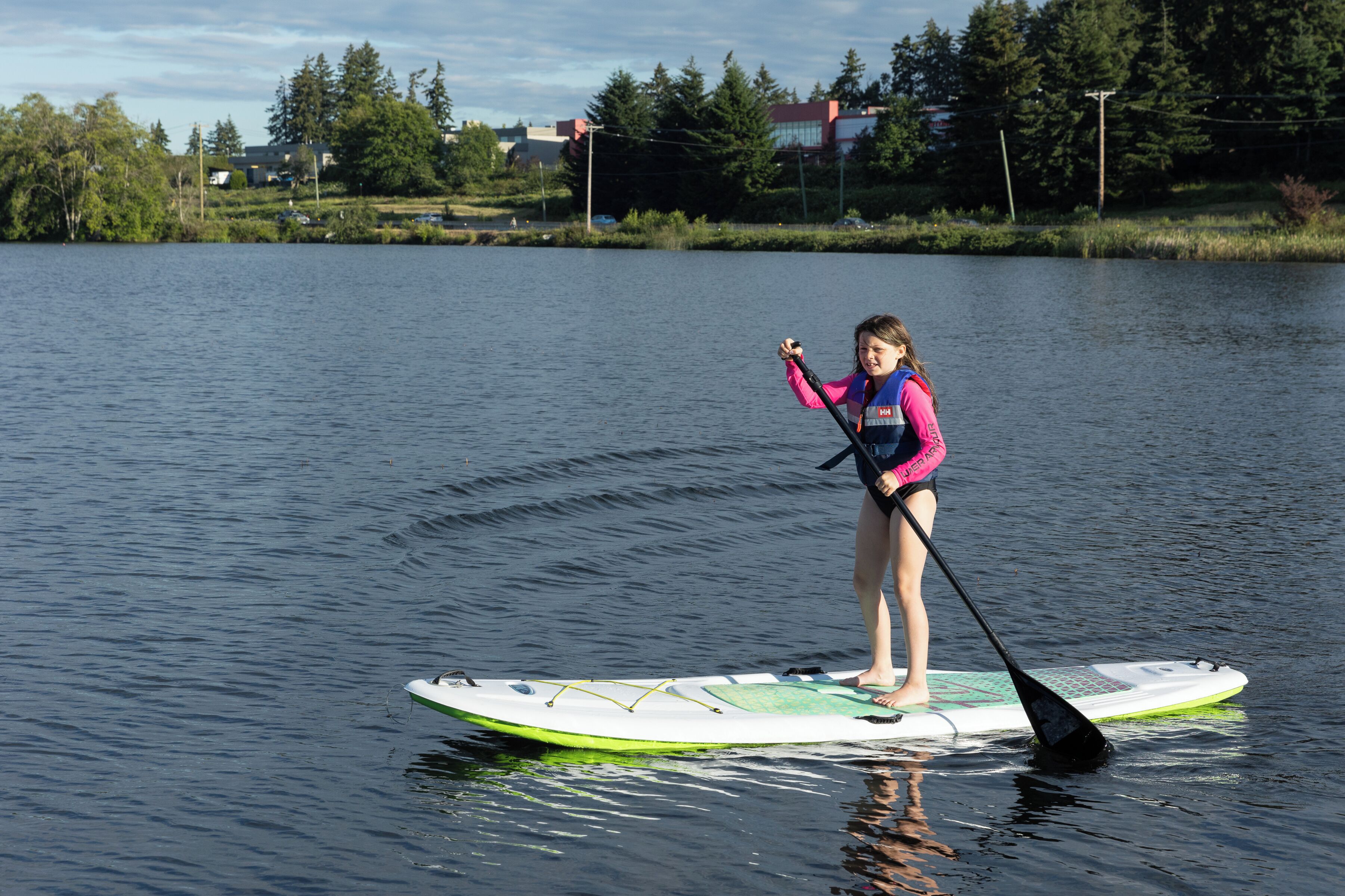 Una persona haciendo paddleboard en un lago tranquilo, con una casa y árboles al fondo.