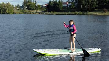 Una persona haciendo paddleboard en un lago tranquilo, con una casa y árboles al fondo.
