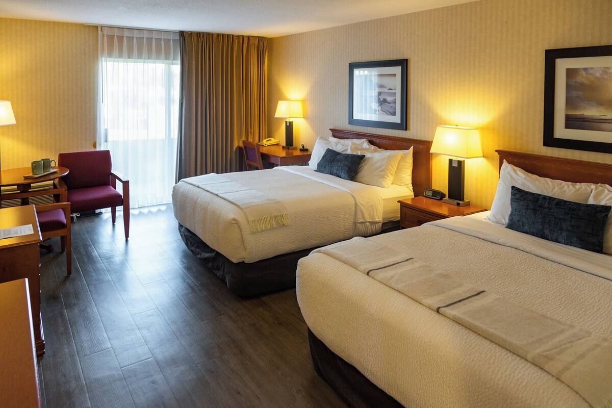 A hotel room with two beds, a desk, a chair, and a window with curtains.