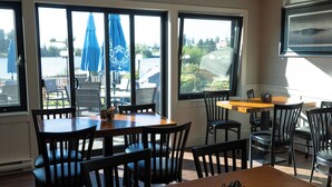A dining area with tables and chairs, large windows with blue umbrellas, and a view of a body of water.