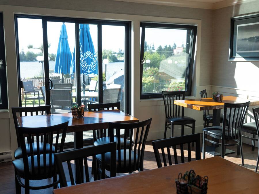A dining area with tables and chairs, large windows with blue umbrellas, and a view of a body of water.