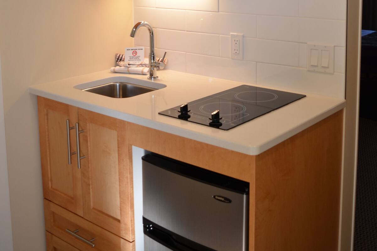 A compact kitchen with wooden cabinets, a stainless steel microwave, a built-in sink, and a refrigerator.