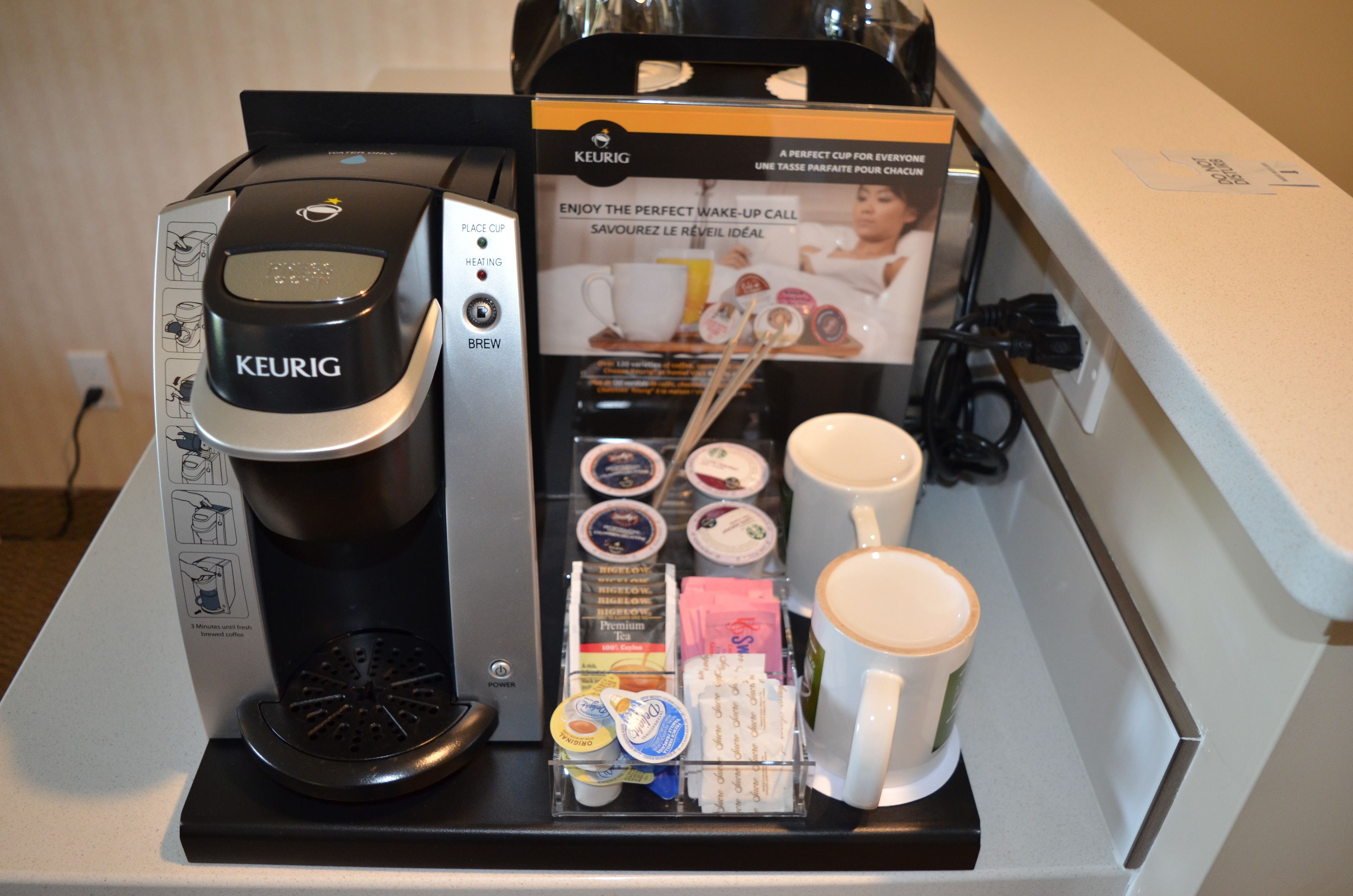 A Keurig coffee machine with a coffee pod holder, a coffee mug, and a box with instructions.