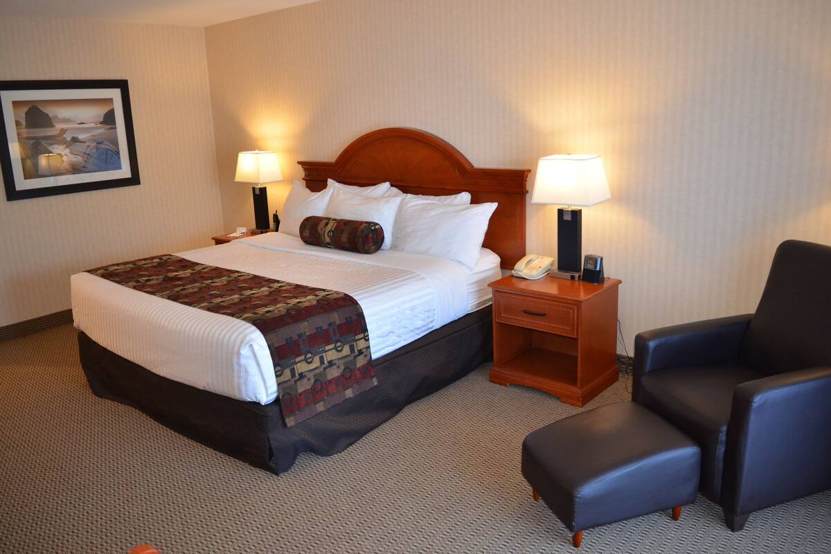 A hotel room with a large bed, two bedside tables with lamps, a chair, and a framed picture on the wall.