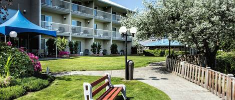 A hotel with a courtyard featuring a bench, a blue canopy, and a well-maintained lawn.