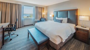 A hotel room with a large bed, a desk, a chair, a bench, and a view of the sea through the window. - The Explorer Hotel Yellowknife (Yellowknife)