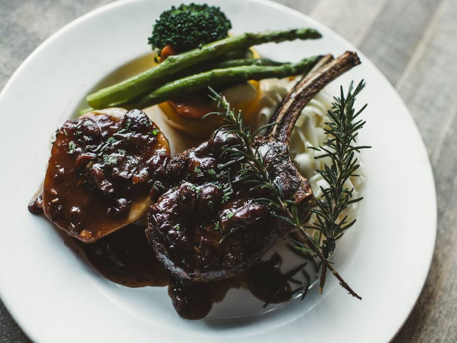 A plate with a lamb chop, asparagus, and a sprig of rosemary.