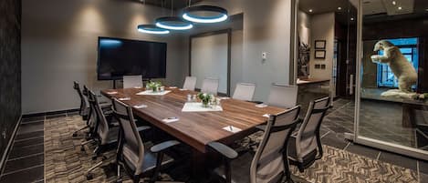 Un salón de conferencias con una larga mesa, sillas, un televisor de pantalla plana y un muro de cristal con una escultura de oso polar.