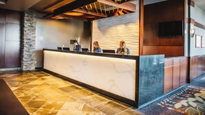 A reception area with a marble counter, a stone accent wall, and a patterned carpet. - The Explorer Hotel Yellowknife (Yellowknife)