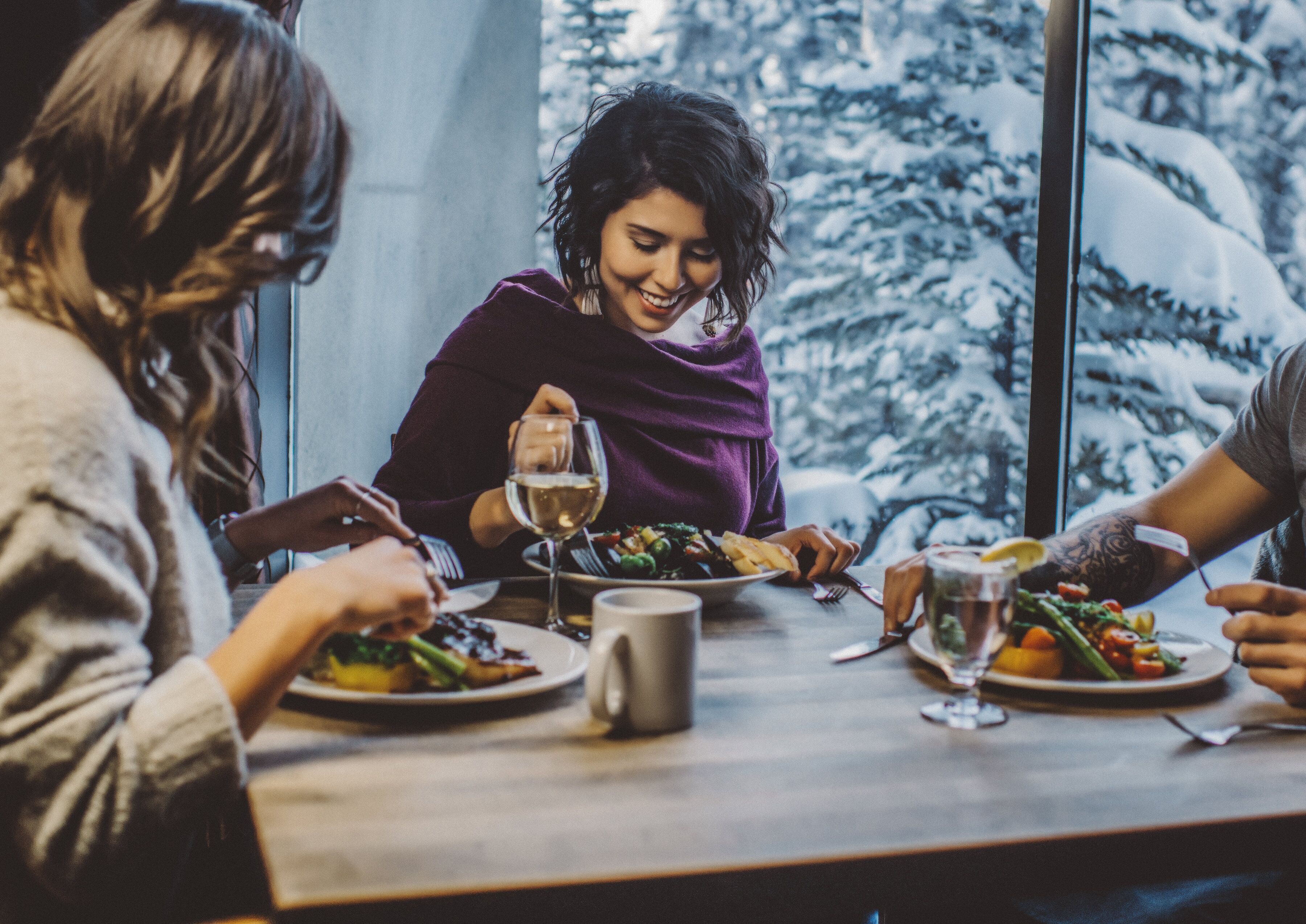 A group of people dining at a table with a view of snow-covered trees through a window.