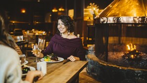 A restaurant interior with a stone fireplace, wooden tables, and dim lighting. - The Explorer Hotel Yellowknife (Yellowknife)