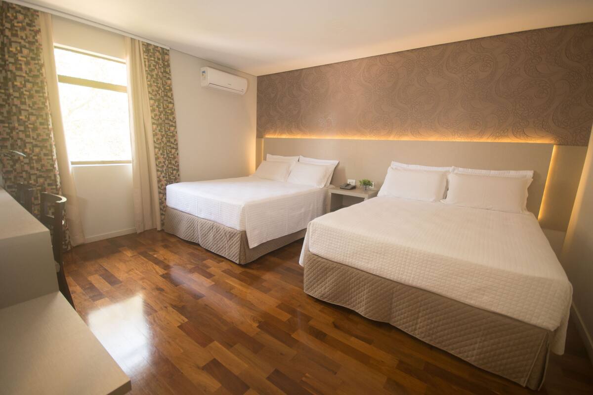 Ein Hotelzimmer mit zwei Betten, Holzboden, einem Fenster mit Vorhängen und einer Wand mit Muster.