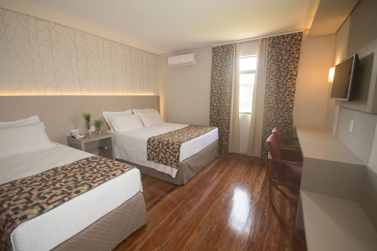 Ein Hotelzimmer mit zwei Betten, einem Schreibtisch, einem Stuhl, einem Fernseher und einem Fenster mit Vorhängen.