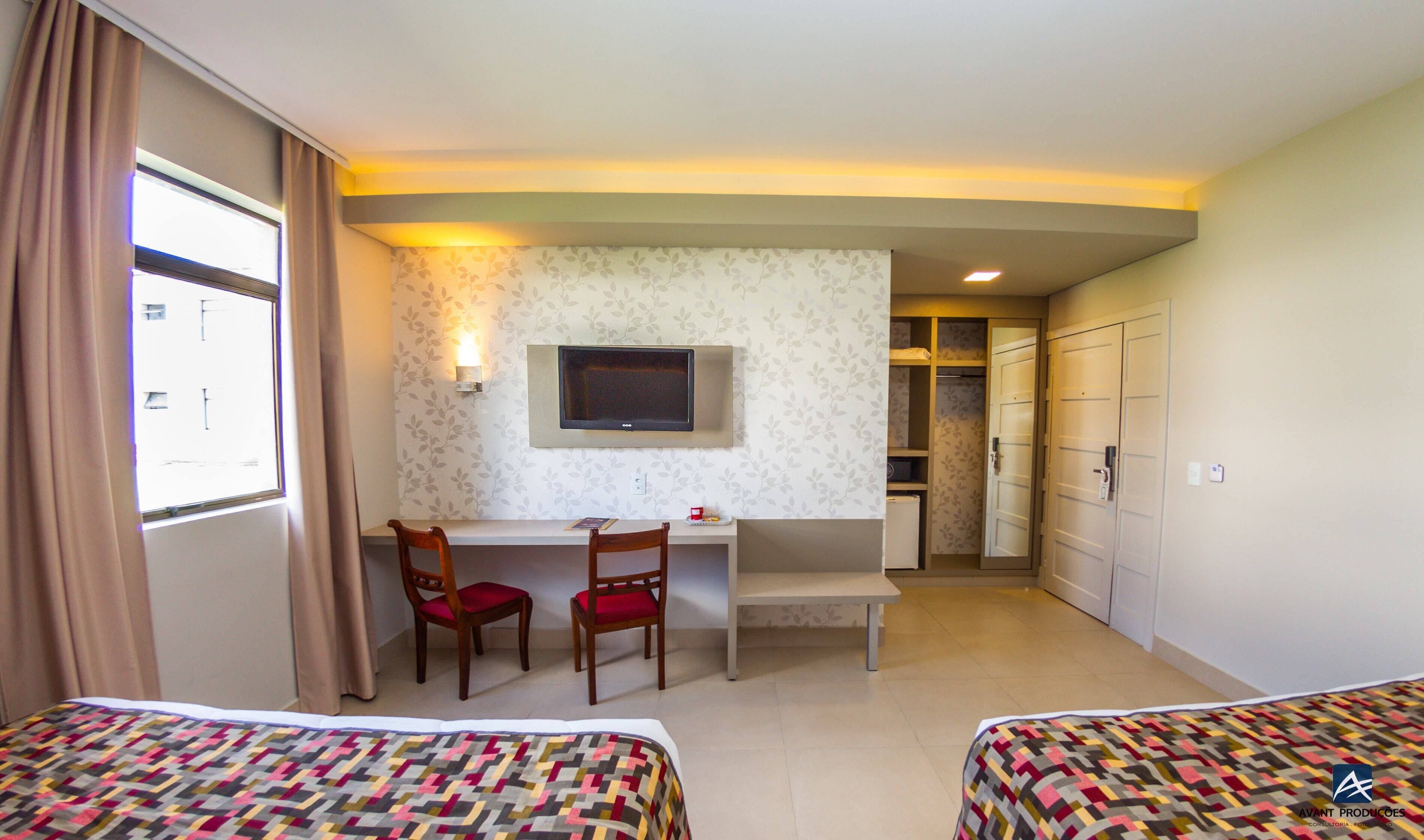 Habitación de hotel con dos camas, un escritorio con silla, televisión y armario.