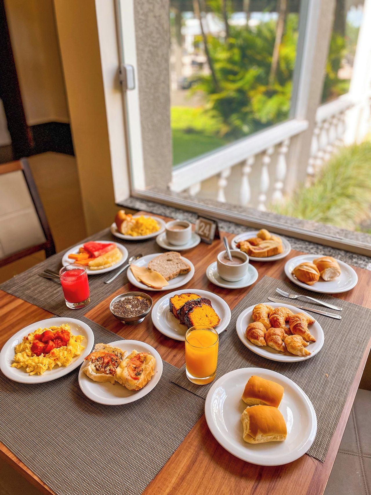 Una mesa de desayuno con diversos platos, como huevos revueltos, tostadas, croissants y un vaso de jugo de naranja.
