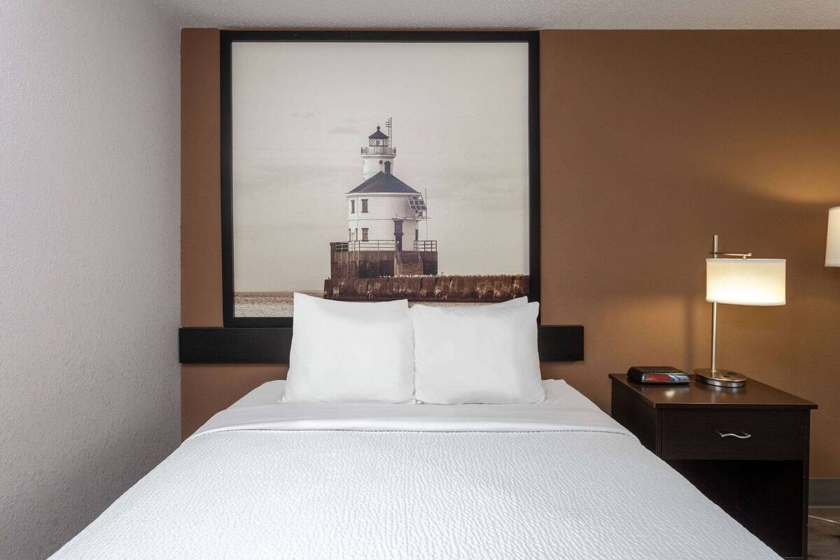 Une chambre d’hôtel avec un lit, une table de chevet avec une lampe et un tableau représentant un phare accroché au mur.
