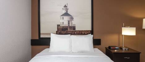 A hotel room with a bed, a nightstand with a lamp, and a framed picture of a lighthouse on the wall.