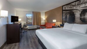 Une chambre d’hôtel avec un grand lit, un bureau avec une télévision, une chaise, un canapé et une fenêtre avec des rideaux.