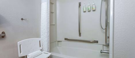A bathroom with a white bathtub, a shower, and a white chair with a towel.