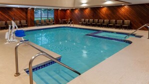 Une piscine intérieure avec un mur en bois servant de décor, une chaise de maître-nageur et un escalier pour accéder à la piscine.