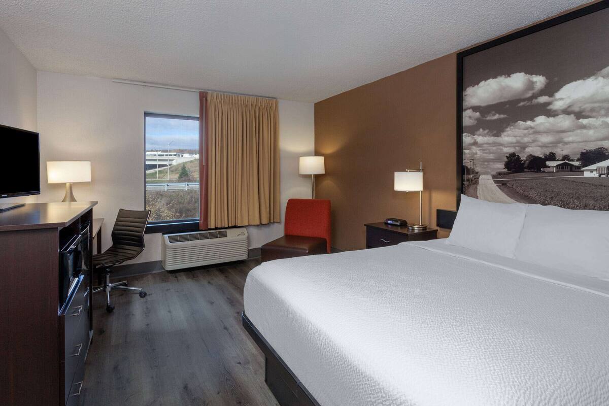 Une chambre d’hôtel avec un grand lit, un bureau avec une chaise, une télévision et une fenêtre avec des rideaux.