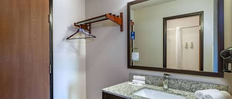 Un baño con puerta de madera, toallero, espejo grande, lavabo y zona de ducha.