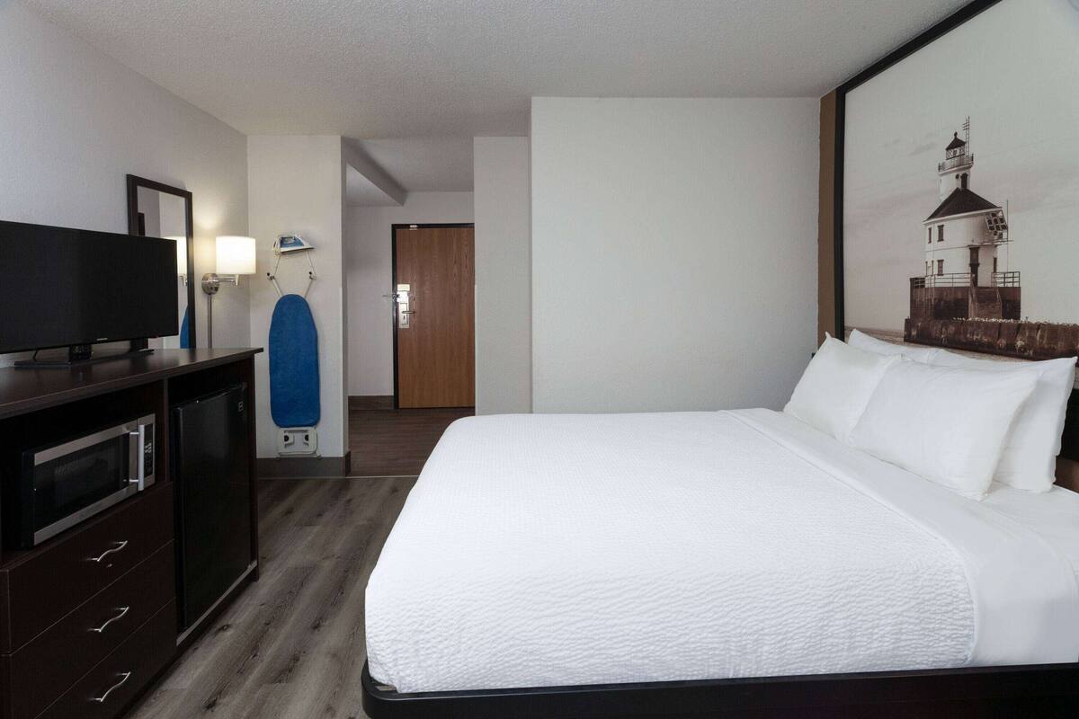 Une chambre d’hôtel avec un grand lit, un téléviseur à écran plat, une commode, un four à micro-ondes et un tableau représentant un phare accroché au mur.