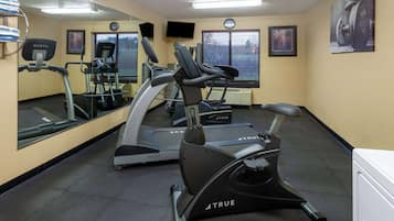 A gym with exercise equipment, a large mirror, and a clock on the wall.