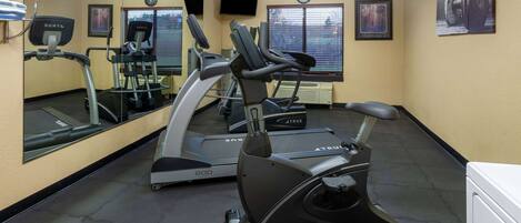 Un gimnasio con equipo de ejercicio, un espejo grande y un reloj en la pared.