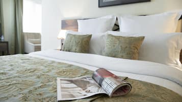 Een net opgemaakt bed met een beddengoed met een patroon, een opgerold tijdschrift op het bed, en een ingelijste foto aan de muur.