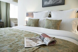 Un lit bien fait, recouvert d’une couvre-lit à motifs, un magazine enroulé posé sur le lit et un tableau encadré accroché au mur.