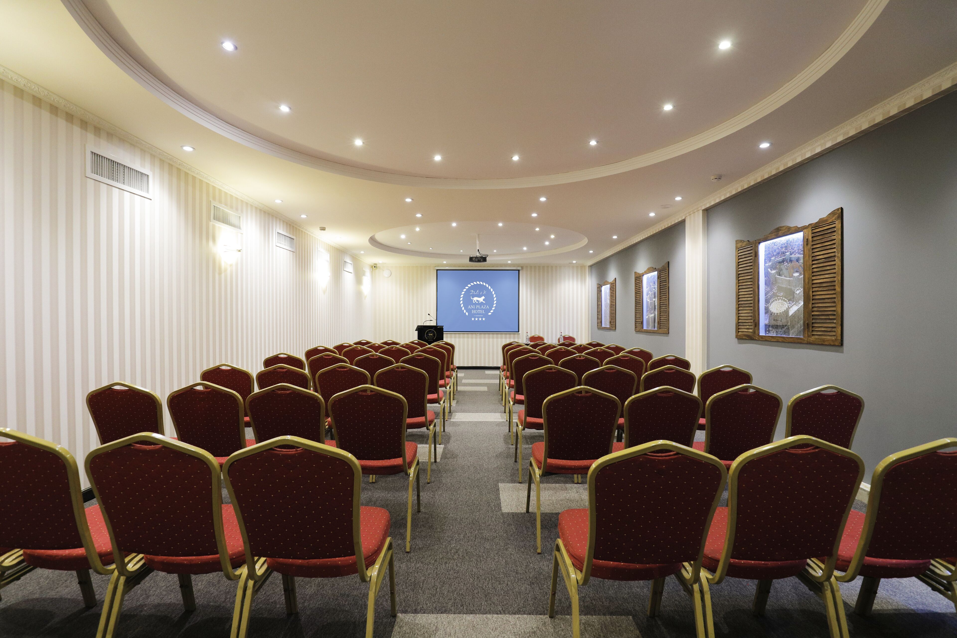 A conference room with rows of red chairs and a large screen at the front.