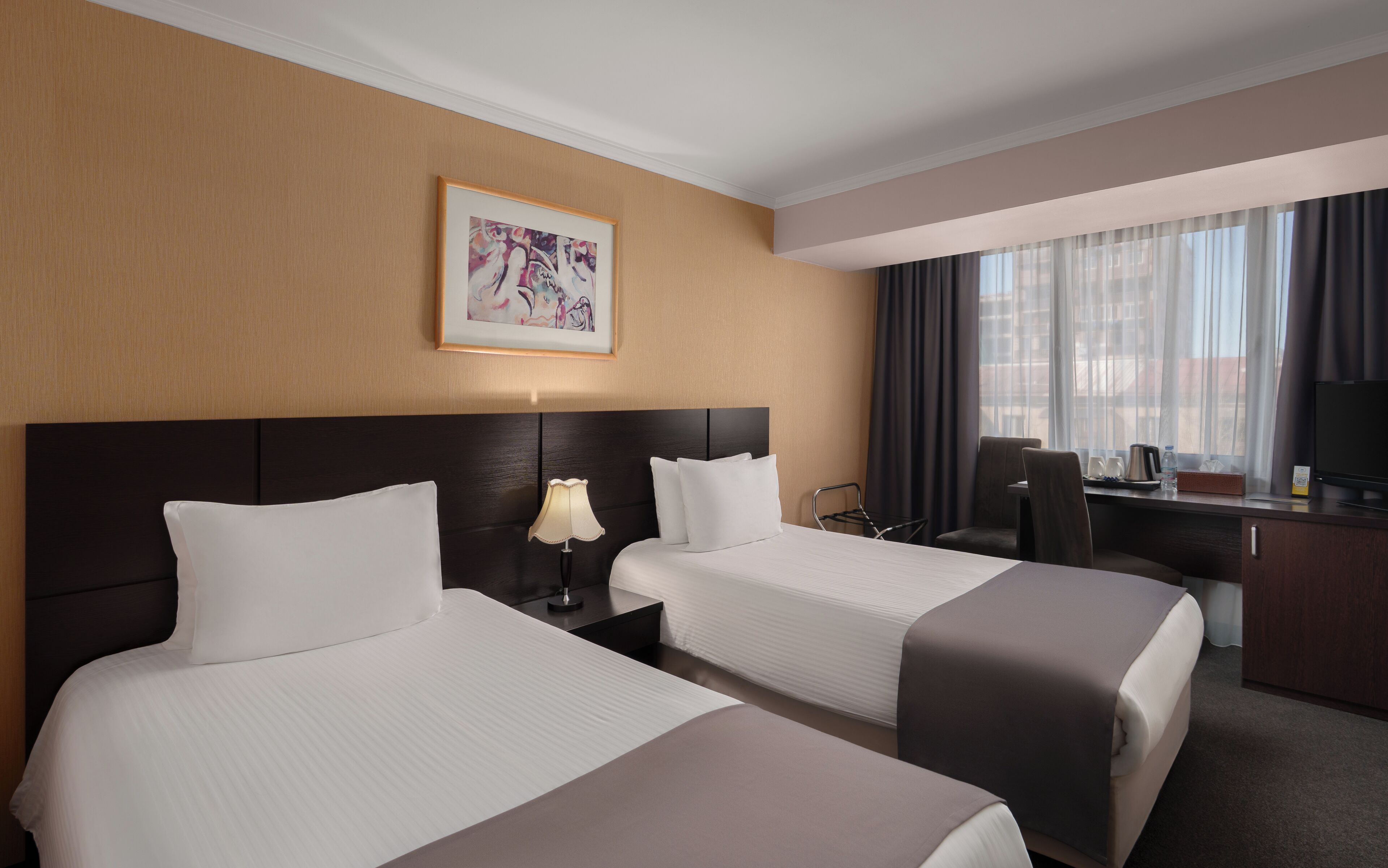 A hotel room with two beds, a desk, a chair, a TV, and a window with curtains.