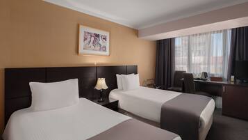 A hotel room with two beds, a desk, a chair, a TV, and a window with curtains.
