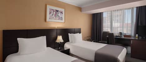 Een hotelkamer met twee bedden, een bureau, een stoel, een televisie en een raam met gordijnen.