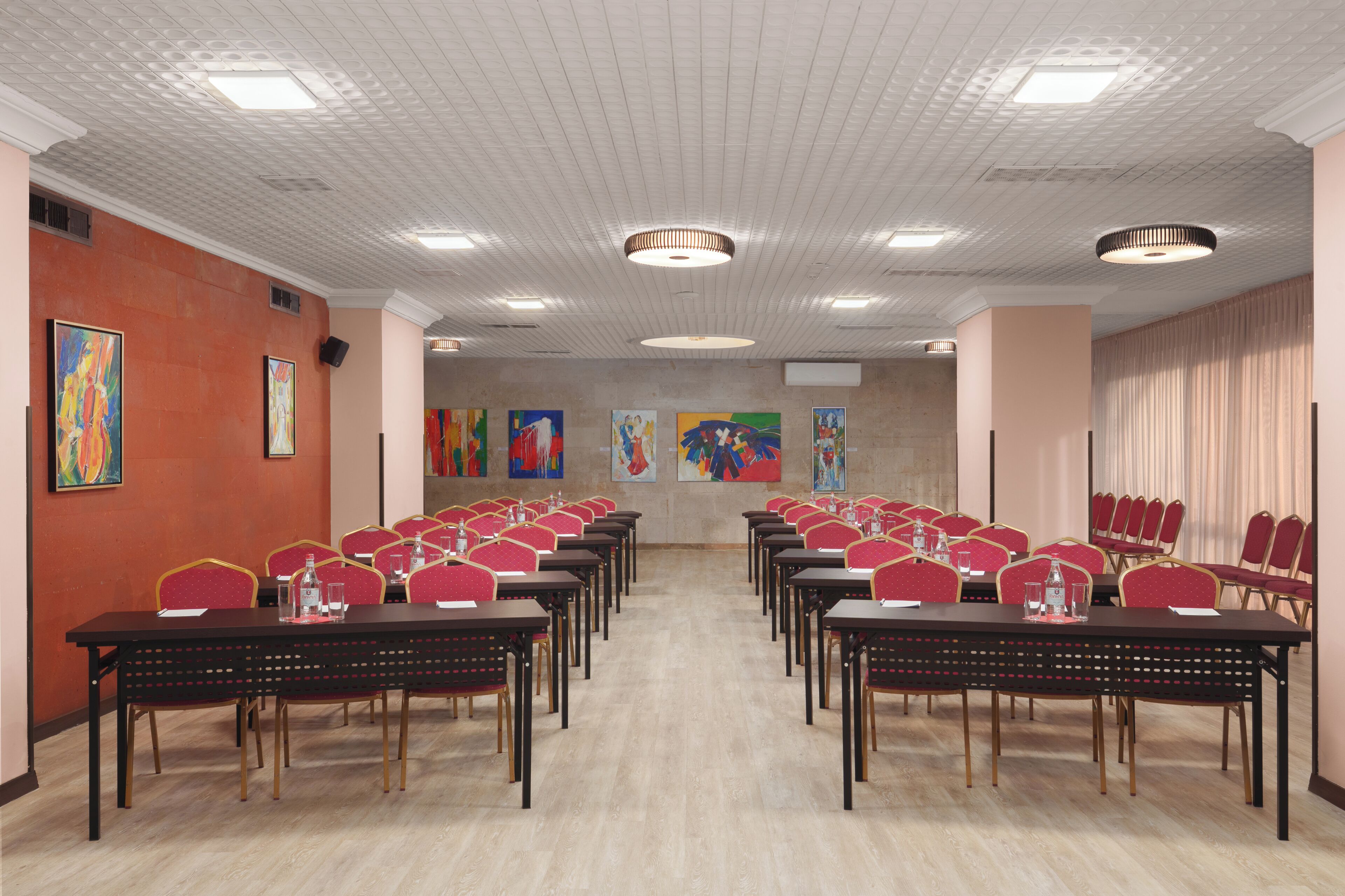 A conference room with multiple tables and chairs, ceiling lights, and artwork on the walls.