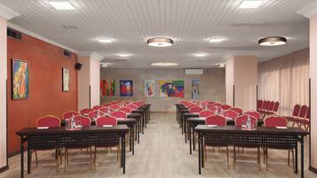 Un salón de conferencias con varias mesas y sillas, luces en el techo y obras de arte en las paredes.