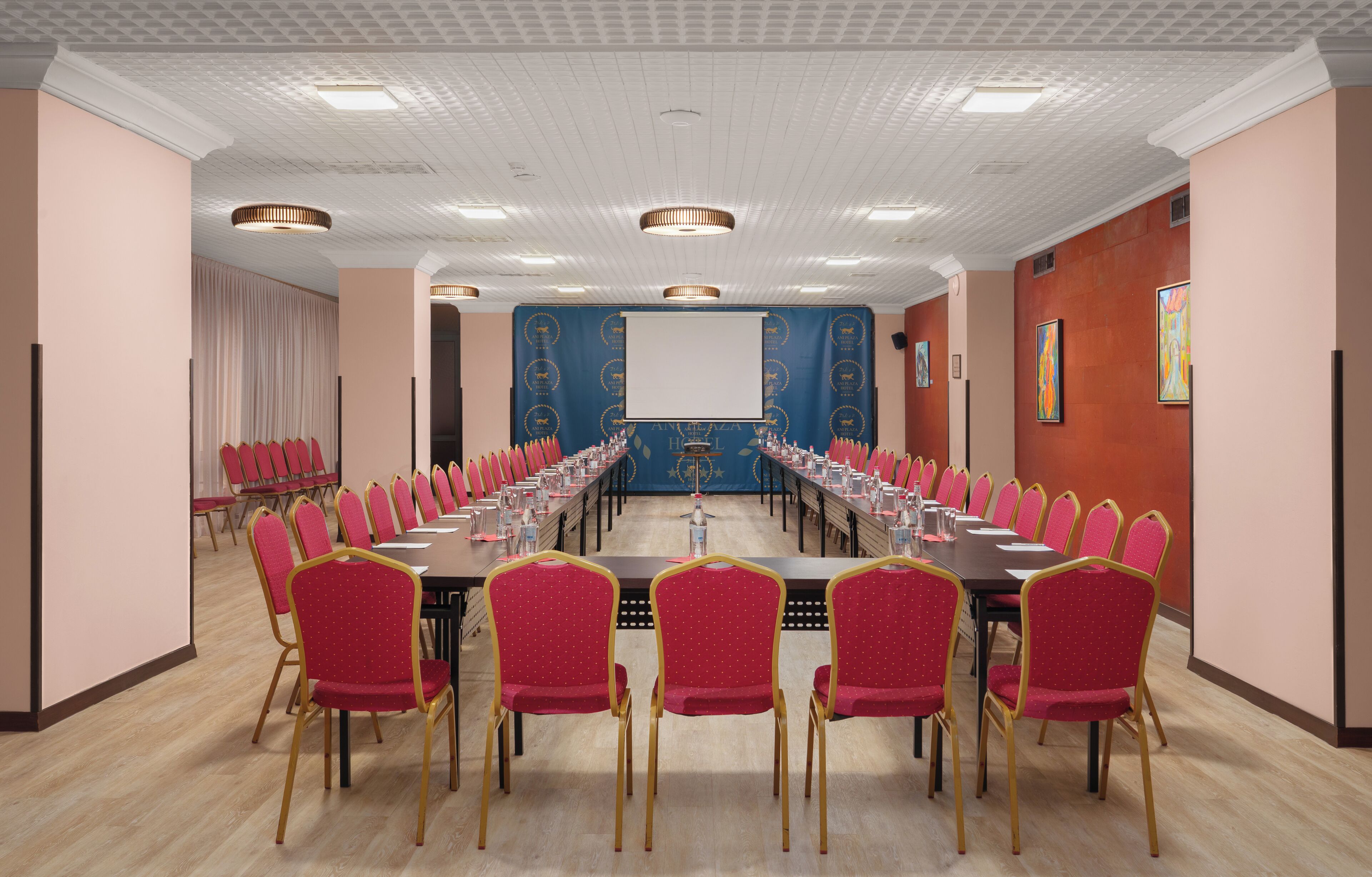 Een vergaderruimte met een lange tafel, rode stoelen, een projectiescherm en een blauwe banner.