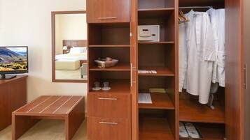 Habitación de hotel con un armario de madera, un pequeño banco de madera, televisión y un espejo que refleja la habitación.